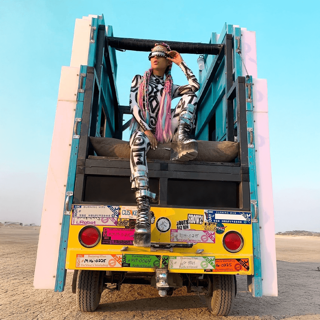 A person in a patterned outfit sits atop a vehicle at Burning Man