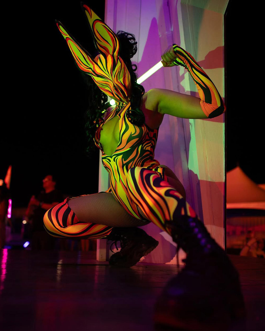 woman wearing a cut-out catsuit while dancing with a glow stick at a music festival